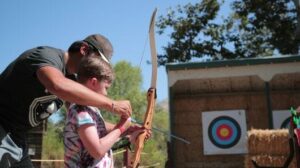 Counselor helping a camper with archery.